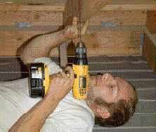 An installer locates the first roof mount by drilling a pilot hole next to a rafter. Other rafters are located from above by measuring off the protruding bit. To prevent leaks, the installer fills the hole with sealant and covers it with the mount.