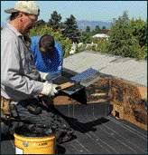 A roofer beds a scupper flashing in roofing cement.