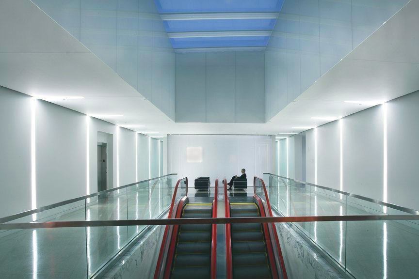 A pair of Schindler escalators, in signature red, face a white accent wall and connect the main and upper levels of the company's headquarters.