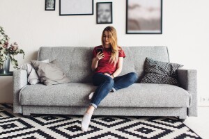 Young woman at home sitting on the couch using smartphone.