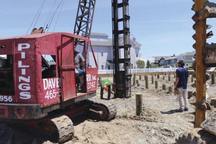 When all the pilings are in their holes, the crew attaches a sled with a 1-ton driving hammer to the crane. The crane positions the sled over each piling and a crew member marks 6-inch increments on the sled to monitor how deep the piling travels with each hit.