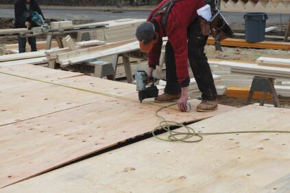 The crew then tacks the sheathing to the studs, using a tape measure to follow the layout.