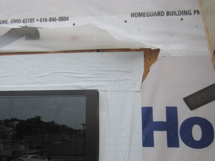 Head flashing. The head flange is covered with a piece of straight peel-and-stick. This flashing must adhere directly to the wall sheathing. Make sure it extends past the outer edges of the window, preferably past the outer edges of the sill flashing tape. The last step is to fold the housewrap back down over the head flashing, and to tape the slits in the housewrap closed.