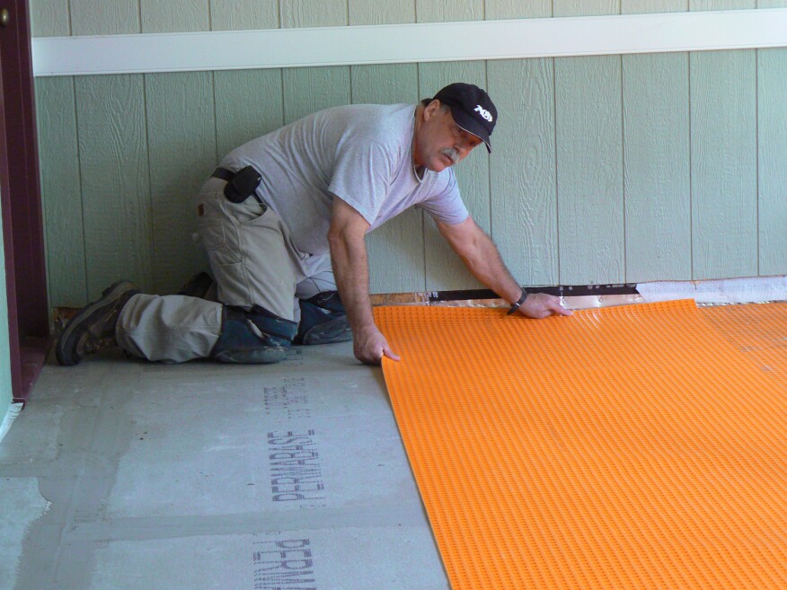 A Schluter-Ditra membrane was used to waterproof and prep the floor for tile. Before installing it, the author cut and dry-fit all the pieces, marking their position with a pencil before rolling them back up, so he would know where to start and stop the thinset while spreading it over the backerboard.