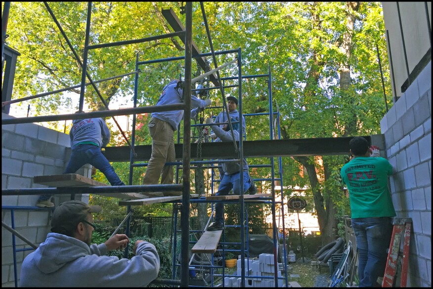 Workers hoist a wall-to-wall steel I-beam lintel in place; the addition’s back wall is opened up to provide as much natural light into the home’s interior as possible.