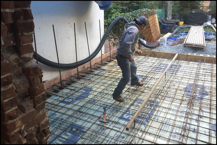 The architect’s initial design called for a crawlspace under a framed first floor supported by block frost walls, but the city’s zoning administrator required slab-on-grade construction. The resulting structural redesign called for a robust 6-inch-thick slab reinforced with two layers of heavy-duty welded wire mesh, the slab tied into the 12-inch-thick-block frost walls with #5 L-shaped rebar placed 12 inches on-center. 2-inch XPS rigid foam was placed over the crushed-stone base, the foam’s seams were taped.