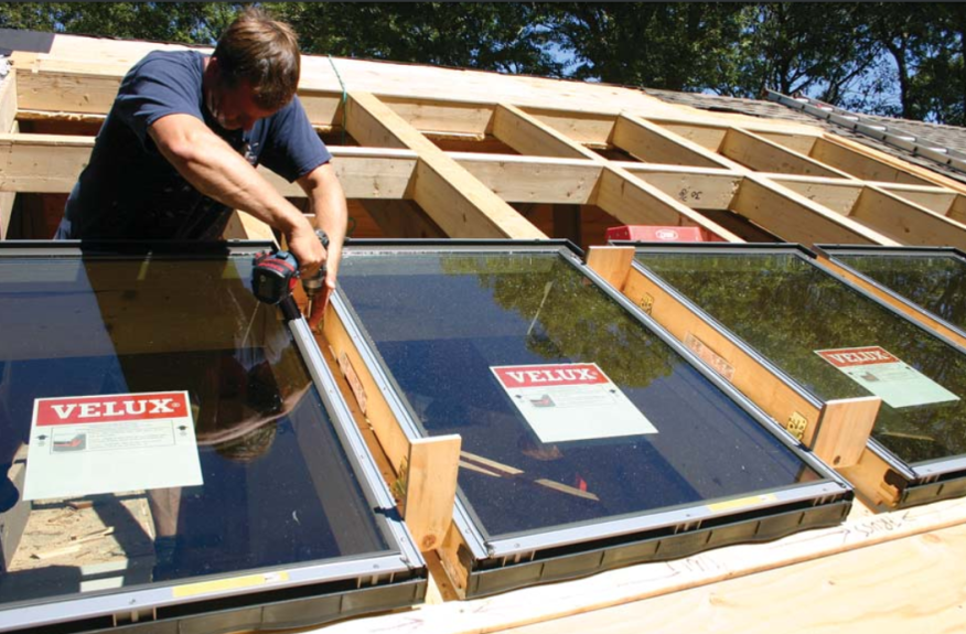 The author laid out the units and the flashing spaces between them on a 1x3 story stick that he nailed to the roof to guide framing. Here, the stick is screwed to a chalk line below the completed rough opening to support and position the bottom row of windows. Plywood gauges ensure accurate spacing between the window frames and prevent dimensional creep.