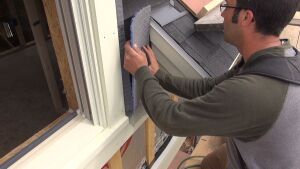 A carpenter applies a woven air-gap mesh to a wall.