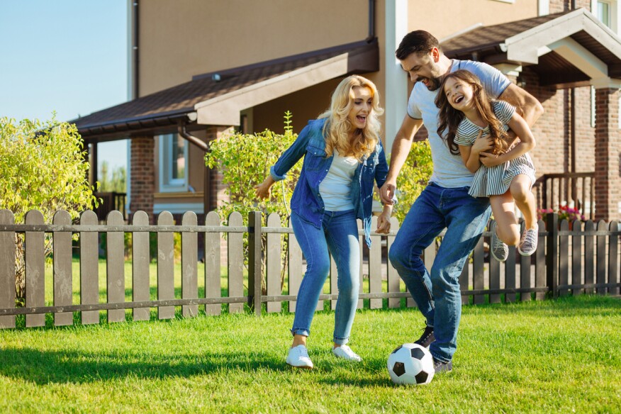 Quality time together. Happy cheerful father carrying his adorable little daughter in his arms while playing football with his family in the backyard