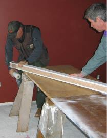With the assembly sandwiched between bending molds, they secure the bundle with plastic stretch wrap to keep it from coming apart as it’s being clamped to the guides on the staircase.