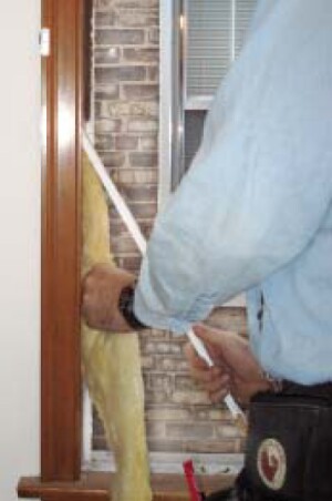 After the old balance system has been removed, the weight pockets are filled with fiberglass. To confirm that the insulation has reached the top of the pocket, the author looks into the hole that previously housed the sash weight pulley.
